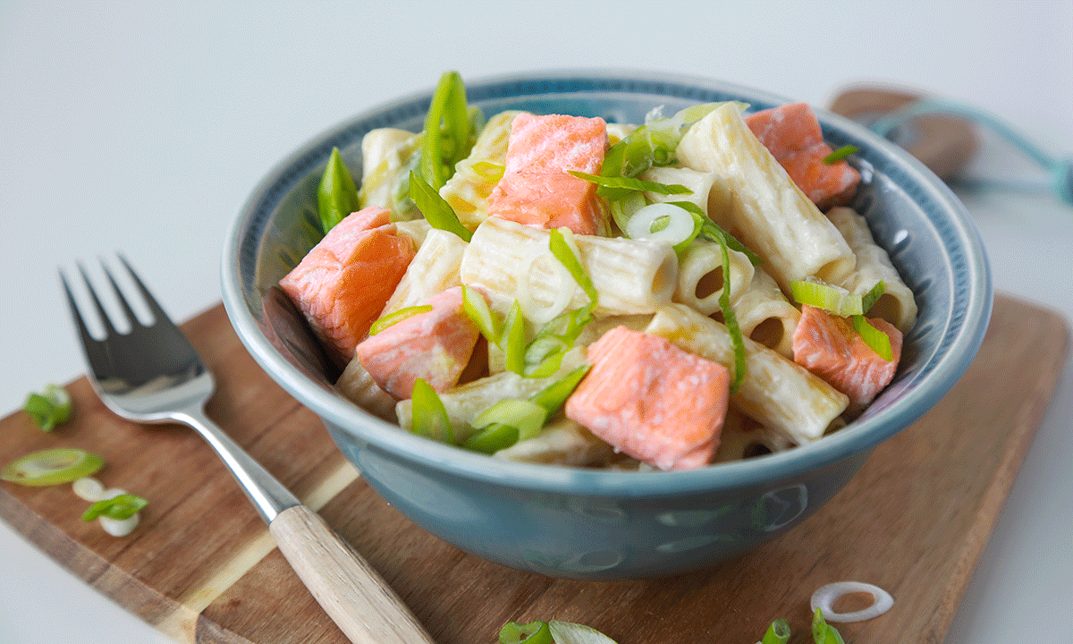 Kremet pasta med laks, toppet med vårløk, i en blå skål