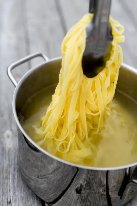Kokt tagliatelle blir dratt opp av kjele med vann, med tenger.