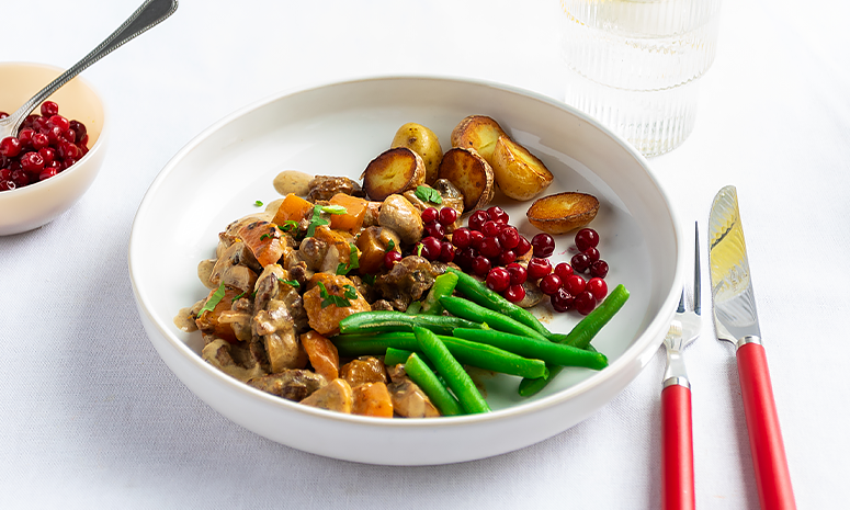 Høstgryte med storfekjøtt, rotgrønnsaker og sopp i en saus servert i en stor hvit skål med kvin og gaffel på siden 