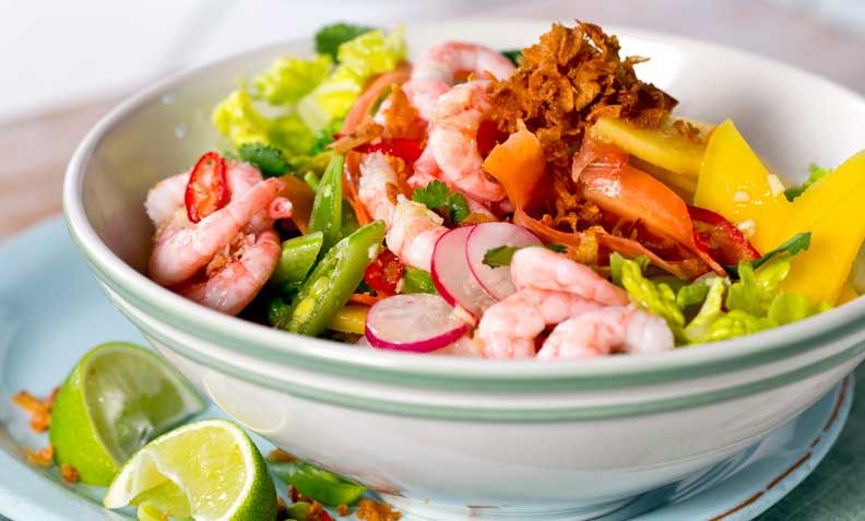 Rekesalat med mango og spicy limedressing, sprøstekt løk og sukkererter i en lys salatbolle.