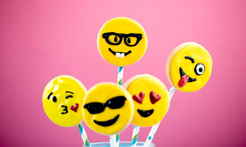 Emoji-kjeks, runde kjeks pyntet som forskjellige gule emojis med diverse uttrykk. Rosa bakgrunn.