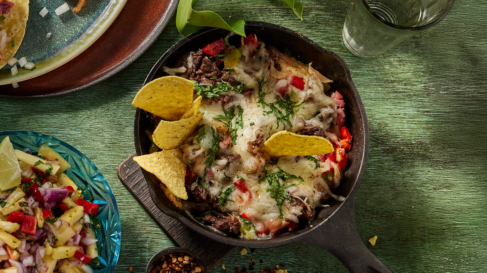 Nachos de alambre – nachos med biff servert i støpejernspanne med tortillachips, og en skål mangosalsa på siden.