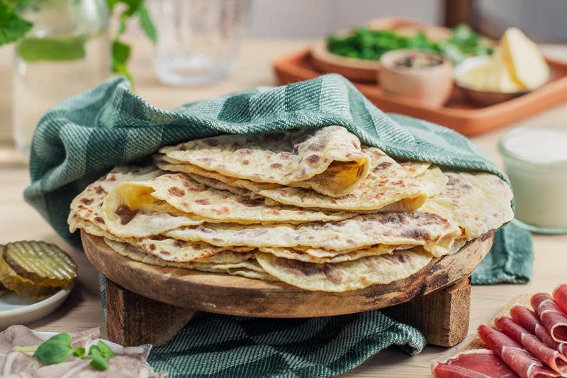 Hjemmelagde potetlefser for nybegynnere servert i stabel under et sjøgrønt kjøkkenhåndkle. Stabelen ligger på et rustikk trefat, omringet av spekemat, sylte og ferske urter.