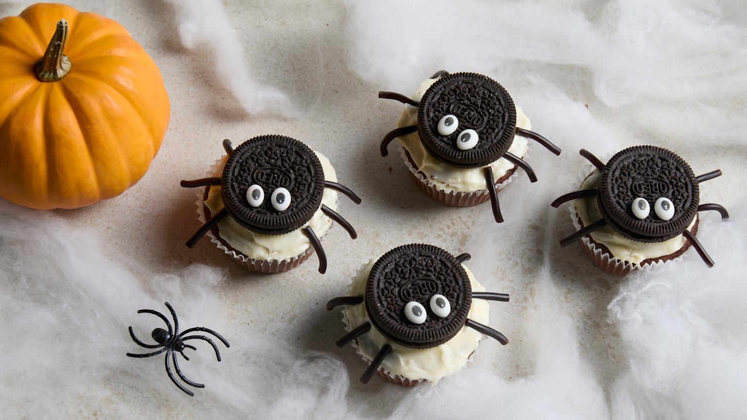 Halloween muffins med kjeks-ederkopper, pyntet med oreokjeks, lakrissnører, øyne og glasur. Lite gresskar, plastederkopp og ederkoppspinn i bakgrunnen.
