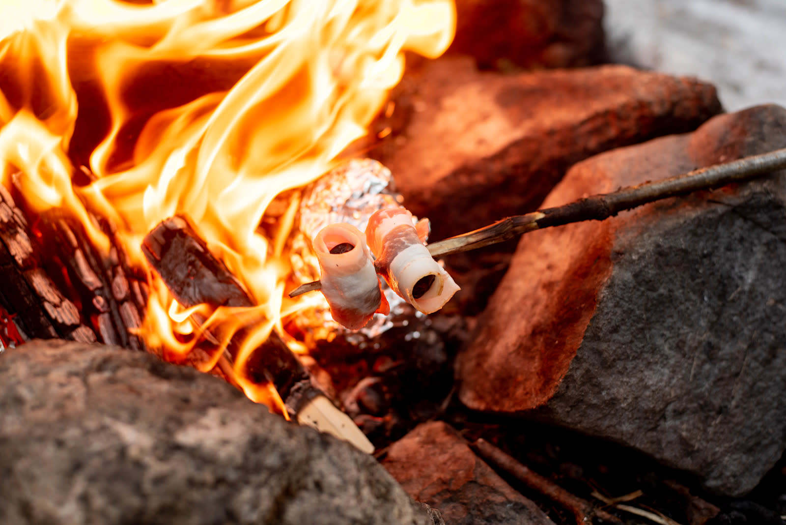 Dadler med bacon - på bålet, stekt på spikket trepinne. Flammer i bakgrunnen.