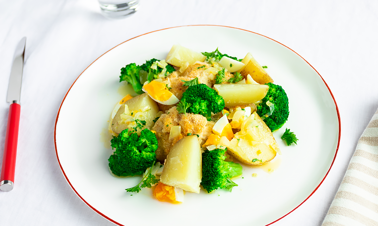 Fiskegrateng med brokkoli, poteter og eggesmør på en hvit tallerken med rød kant.