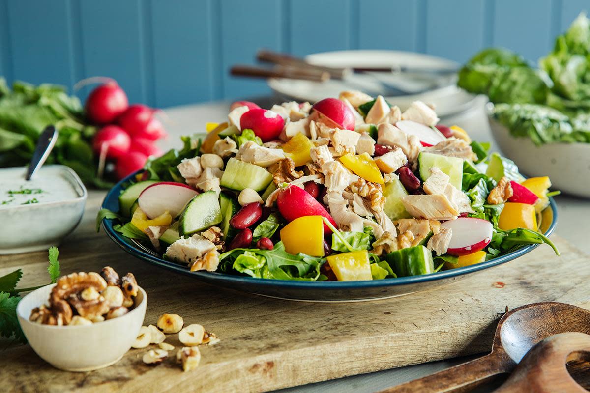 Fargerik kyllingsalat med grillet kylling, paprika, agurk, kidneybønner, reddik og ruccola. Servert på sjøgrønt fat, på trefjøl, med ferske råvarer rundt.