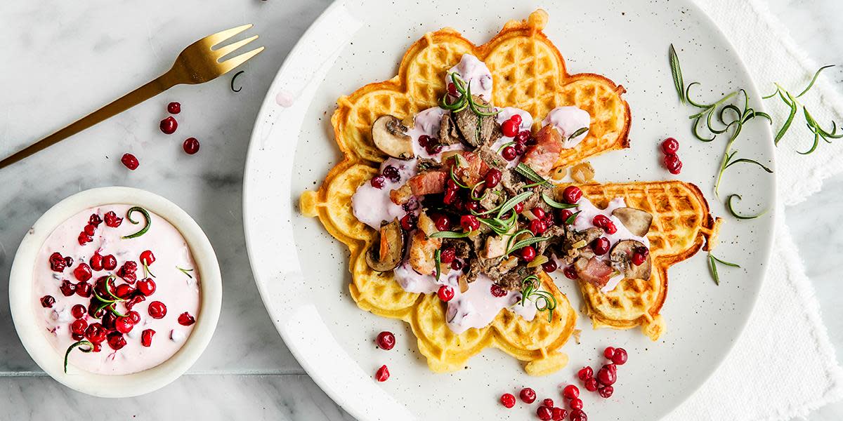 Potetvaffel med trollkrem og reinskav, servert på hvit tallerken, på marmorplate. Fersk rosmarin og en skål trollkrem på siden.