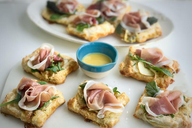 Butterdeigsterter med pære og pepperbrie servert på hvitt fat. Toppet med babyleaf og spekeskinke. Sennepsaus i liten blå skål ved siden av.