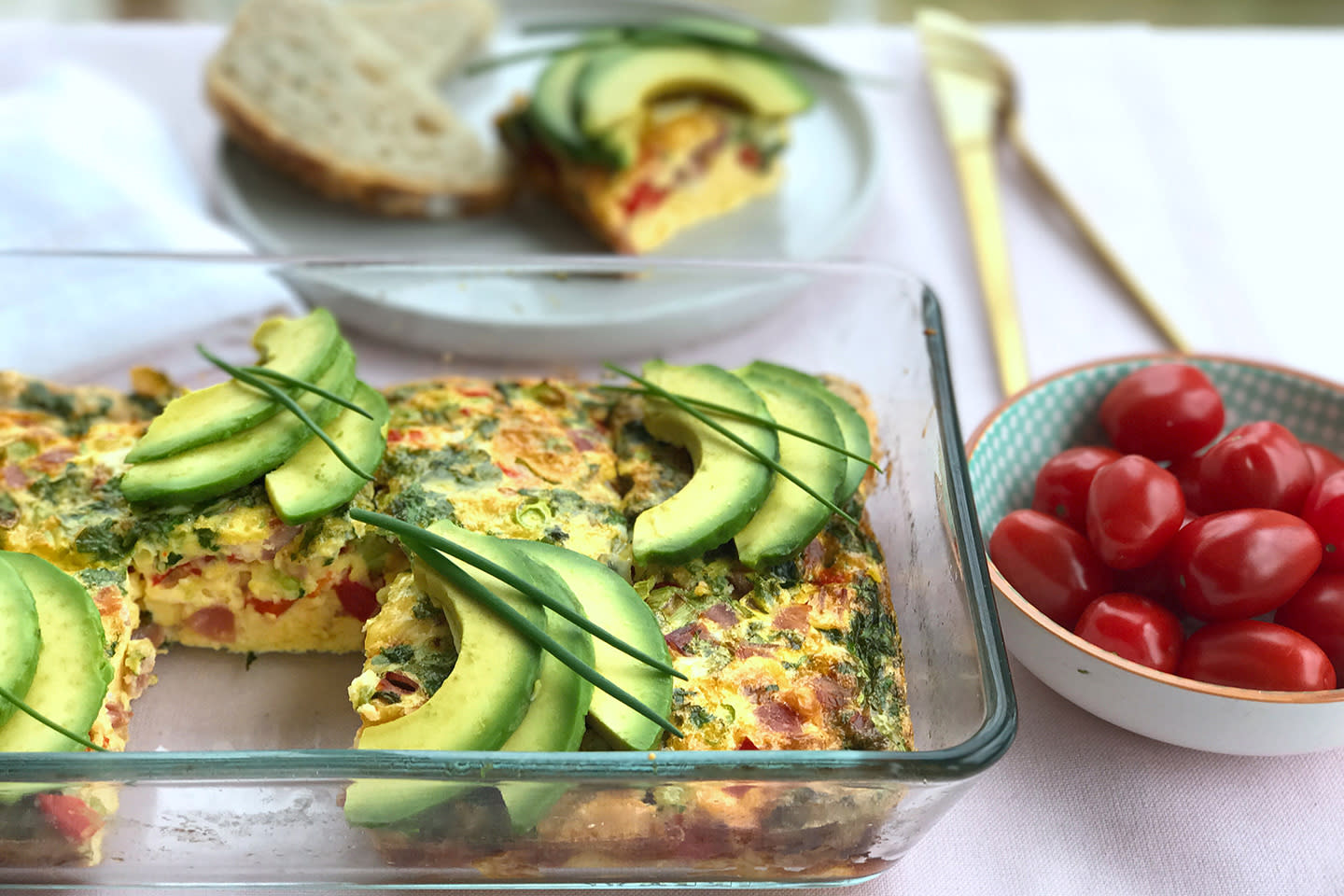 Ovnsbakt omelett i glassform med skivet avokado og gressløk på toppen. Plommetomater i skål ved siden av.