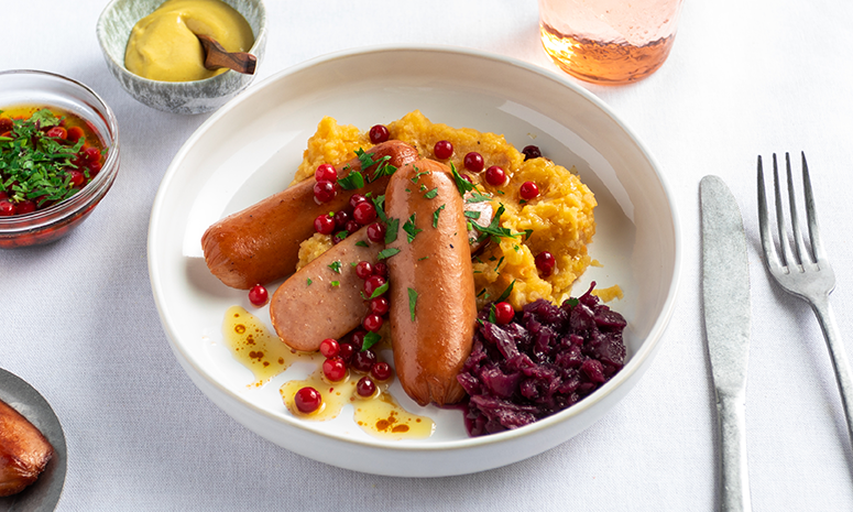 Kjøttpølser med kålrotstappe og brunet smør servert i dyp hvit tallerken med rødkål og tyttebær.