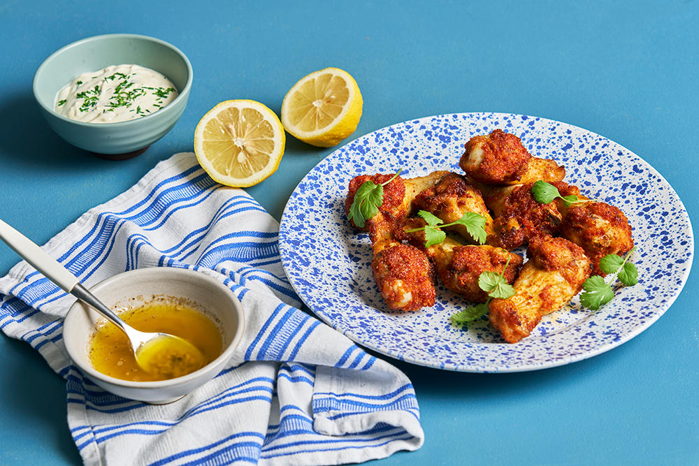Coop Crispy hotwings med lemon pepper saus og ranch dip servert på blåflekkete hvit tallerken med skåler med tilbehør rundt.