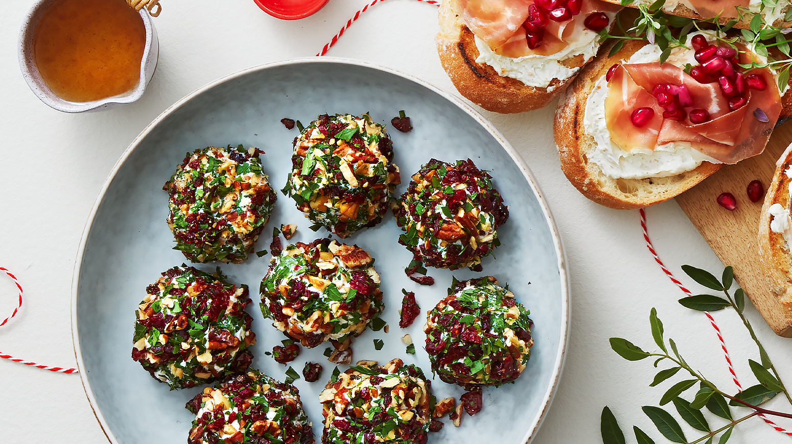 Ostekuler med nøtter og tranebær, rullet i persille og servert på lyseblå tallerken på tapasbord med juletema.