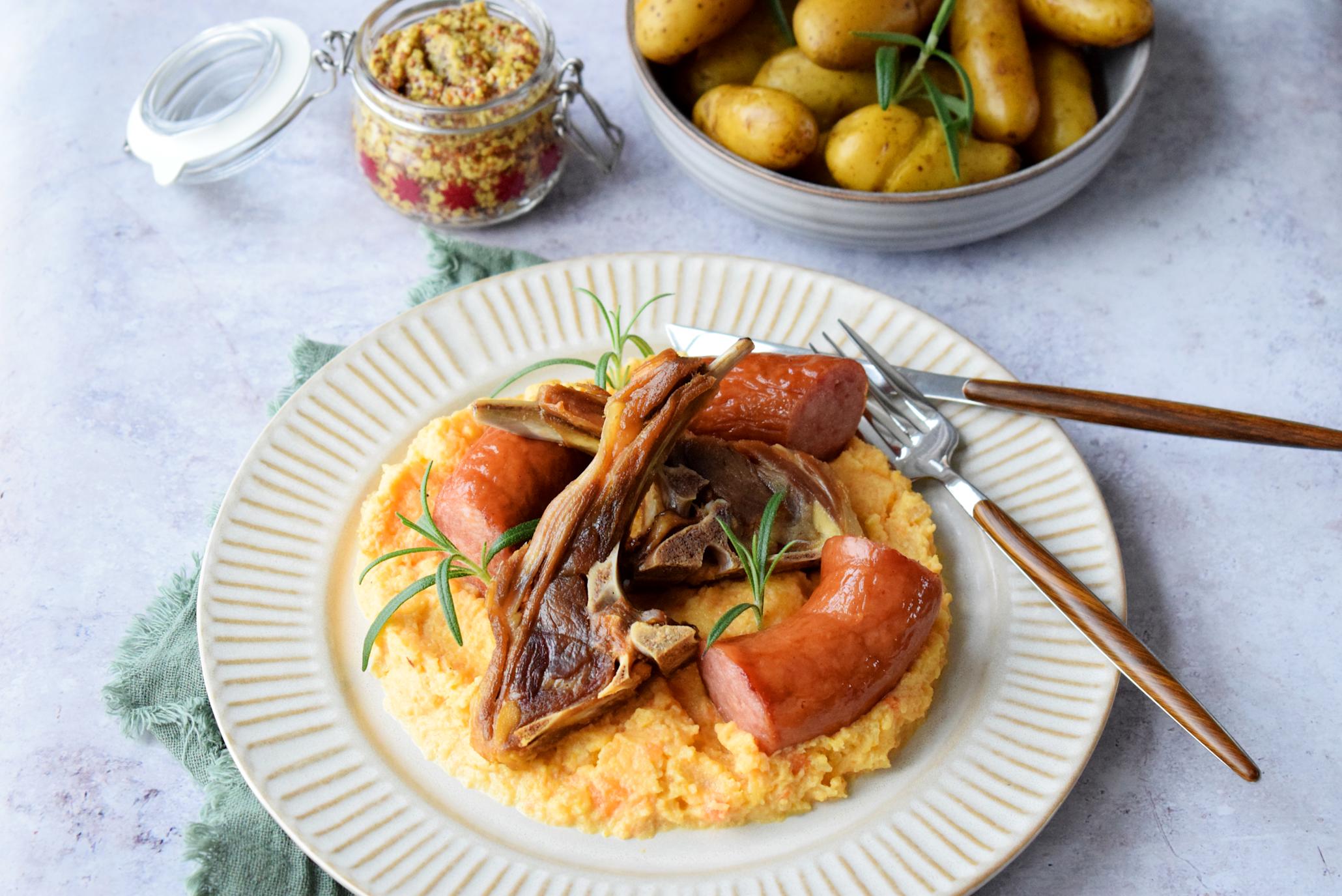 Tradisjonelt dampet Xtra pinnekjøtt på lys tallerken med hjemmelaget kålrabistappe, biter av vossakorv og fersk rosmarin. Poteter og grov sennep på siden.