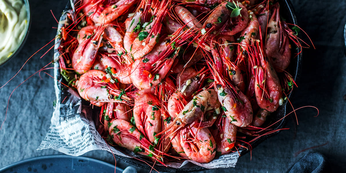 Spicy reker med skall, servert i skål med avispapir på mørk linduk. Skål med majones ved siden av.