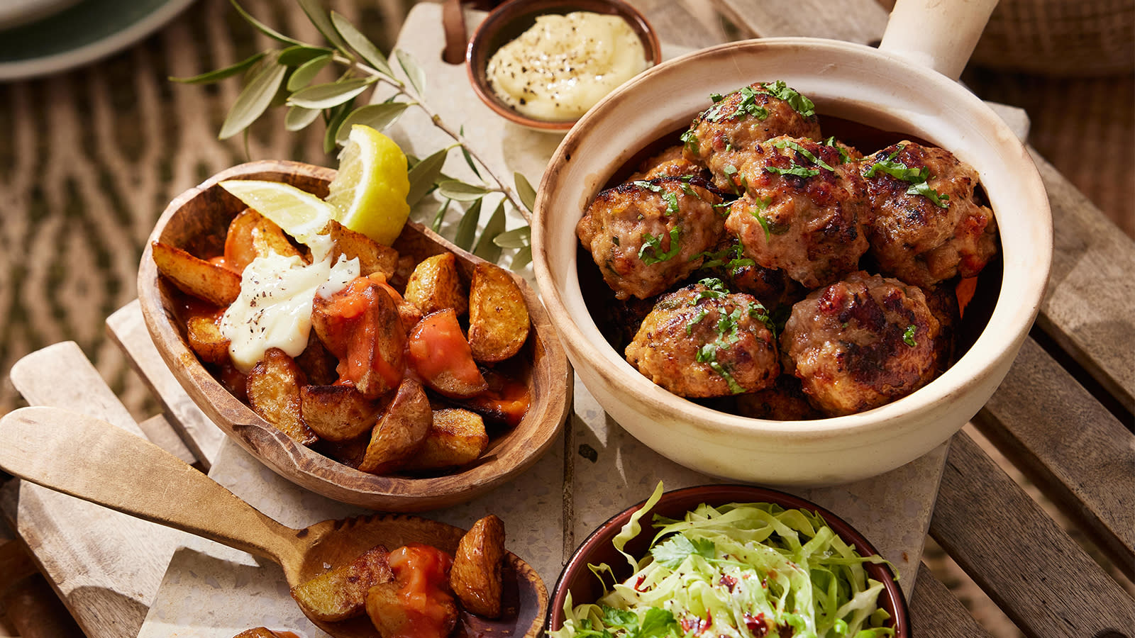 Albóndigas med patatas bravas servert på rustikk bord med aioli og sitronbåter.