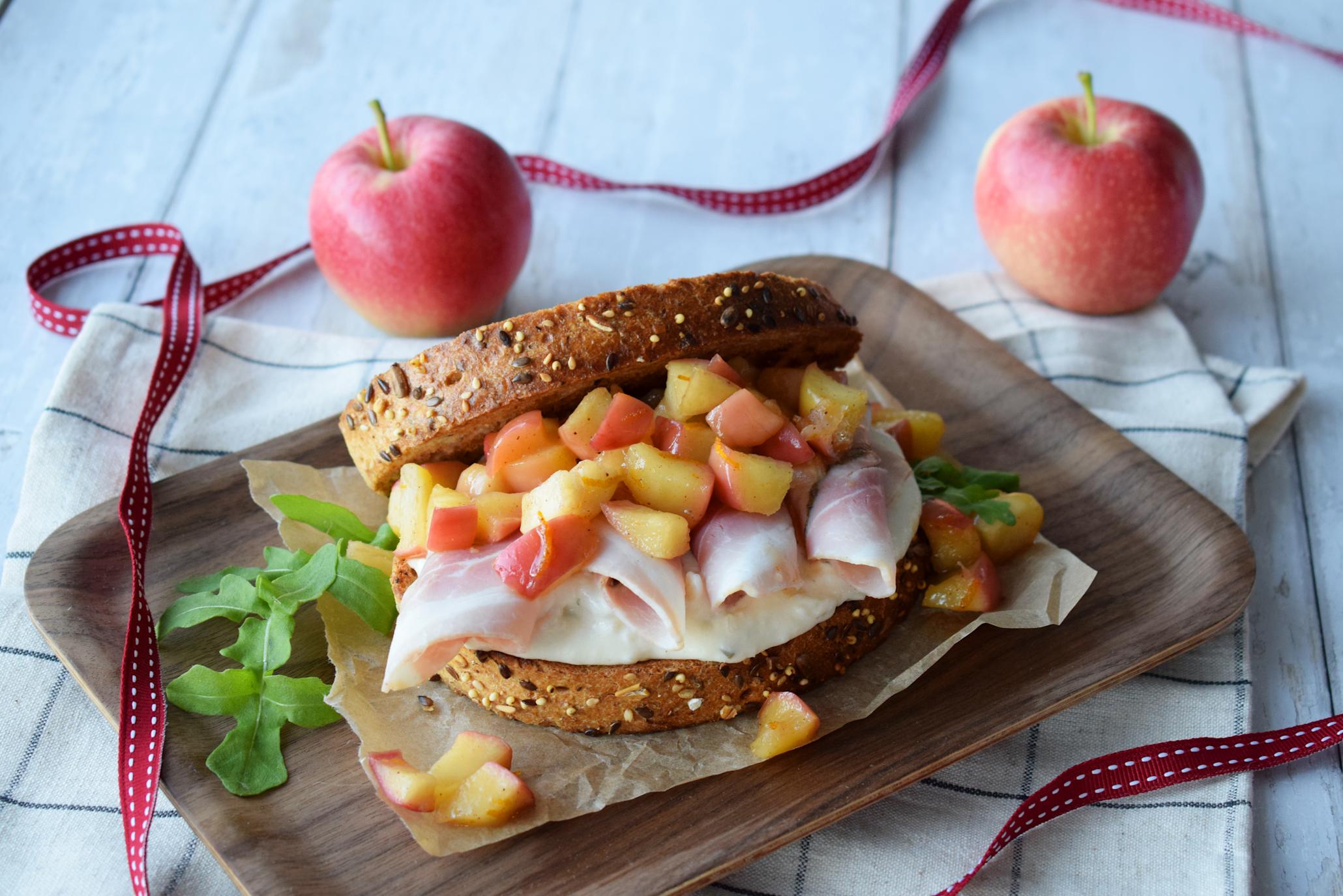 Julesandwich med Xtra ribberull, Xtra potetsalat, grovt brød og honningstekte eplebiter med appelsinskall, på mørk trefjøl. Hvit trebakgrunn.