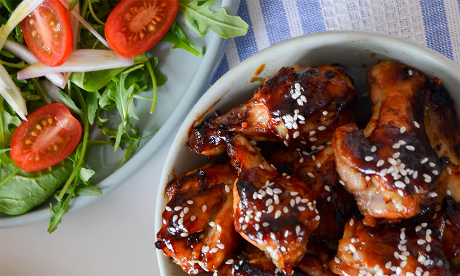 Kylling teriyaki med sesamfrø i en hvit skål ved siden av en hvit skål med ruccola, tomater og løk.