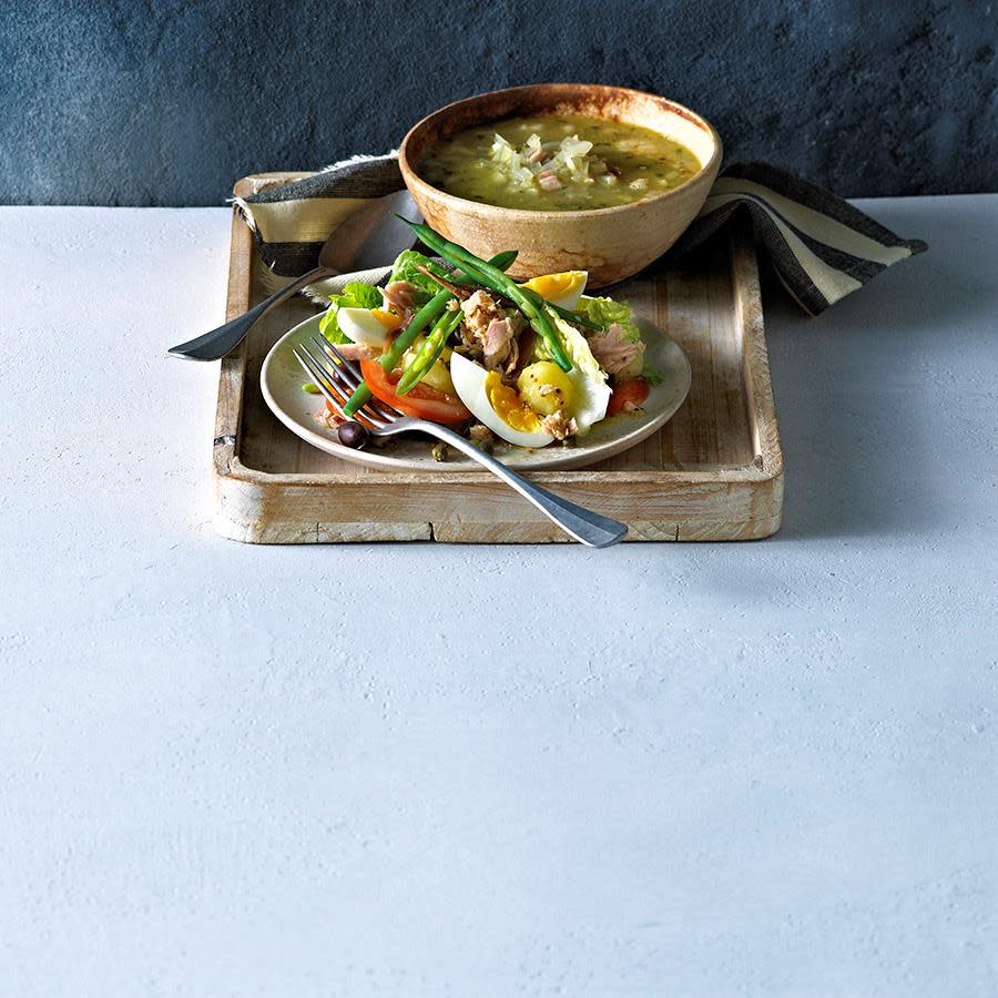 Salat nicoise med kokt egg, tunfisk og grønne bønner servert på hvit tallerken på rustikk trebrett sammen med suppe.