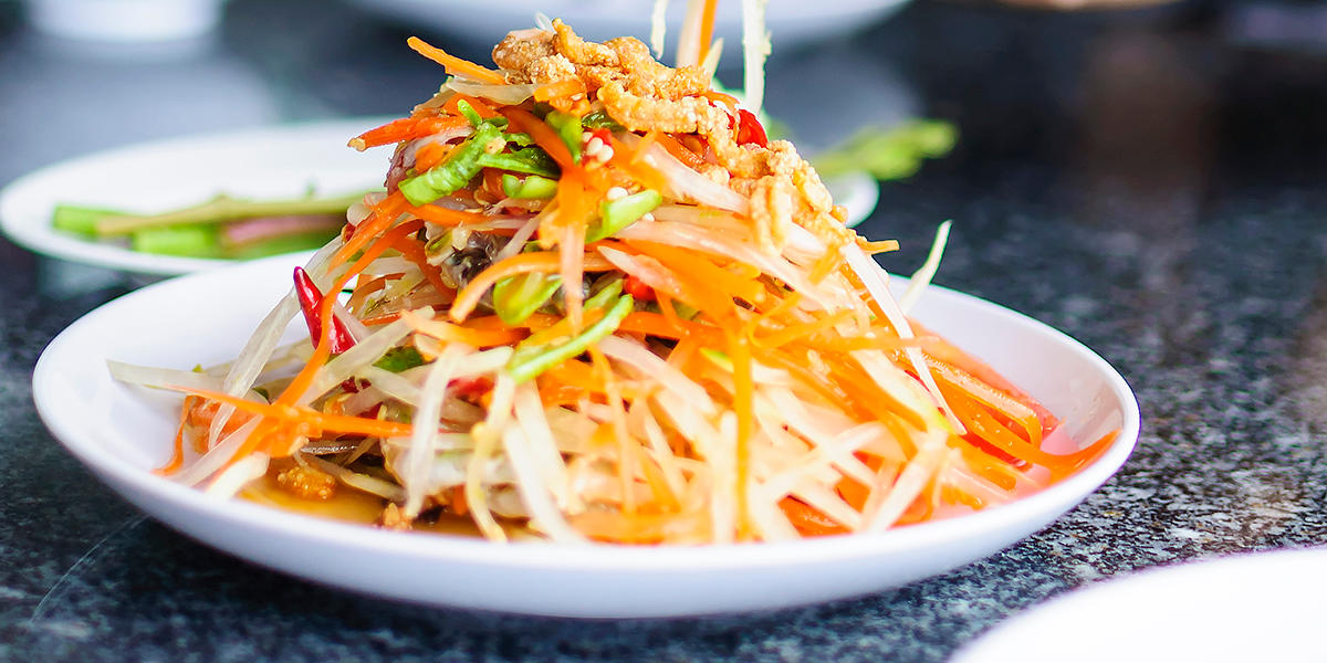 Skål med asiatisk nudelsalat med grønnsaker og chili i tynne strimler. Salaten er toppet med dressing og peanøtter.