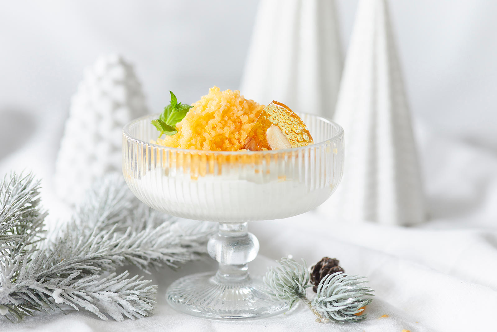 Frossen klementin med honningpisket mascarponekrem servert med mandelknekk og friske mynteblader i iskremskål. Hvit julepynt rundt.