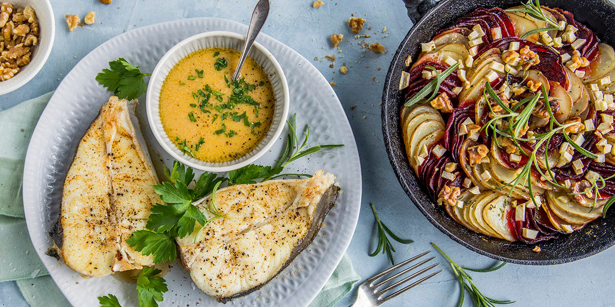 Pannestekt kveite med beurre blanc og potet- og rødbeteform. Kveiteskivene er servert på hvit tallerken med friske urter og en skål beurre blanc, potet- og rødbeteformen er servert i svart ildfast form med ferske urter på toppen.