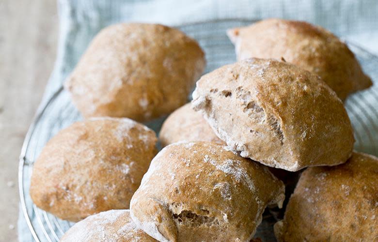 Halvgrove turstykker, rundstykker med fullkornshvetemel, servert på rund kjølerist med lyseblått kjøkkenhåndkle under.