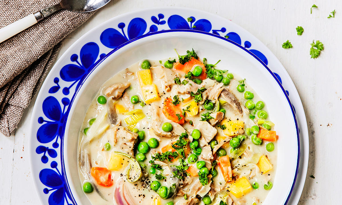 Lammefrikassé med gode grønnsaker servert i hvit skål med mørkeblått mønster. Fersk kruspersille strødd over, og bestikk på siden.