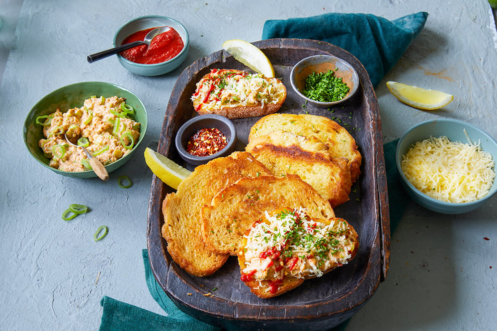 Krabbetoast servert på ovalt trefat, med små skåler krabberøre, chiliflak, revet østavind og rød saus rundt.