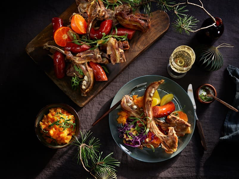 Øldampet pinnekjøtt servert på mørk tallerken på dekket bord, med pølse, rotmos, gulbeter, klementin og rødkål.