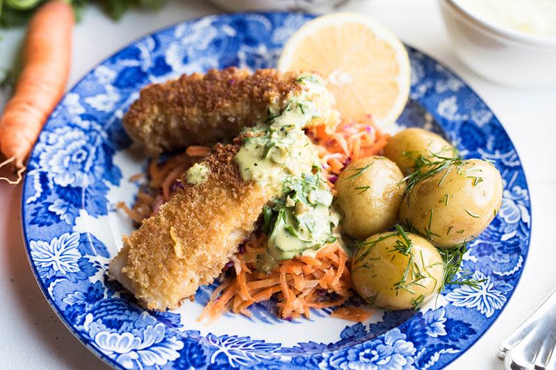 Hjemmelagede fiskepinner med remulade og råkost, poteter og sitronskive på hvit og blåmønstret tallerken.