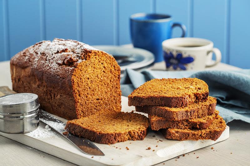 Saftig krydderkake bakt i brødform, servert med et dryss melis på lys trefjøl på dekket kaffebord.