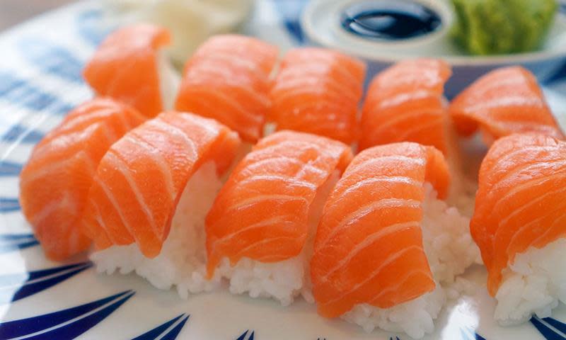 Ti sushibiter med laks på toppen ligger på hvitt og blåmønstrert fat.