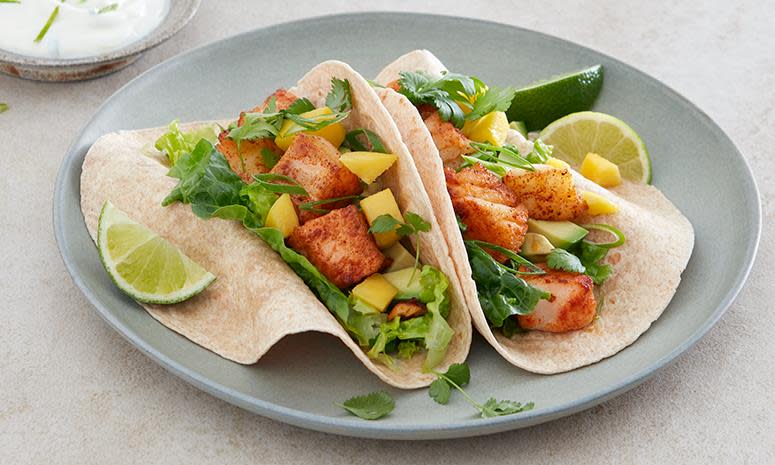 Fisketaco med laks og torsk i biter, tacolefse, mango, ferske urter og limedressing på grå tallerken. Lys bakgrunn.