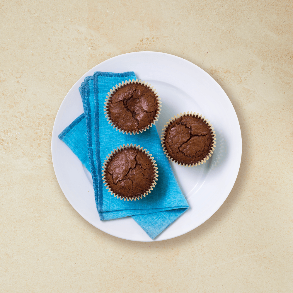 3 sjokolademuffins på en hvit tallerken, med et blått håndkle under