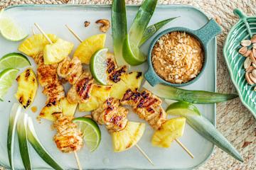 Grillet ananas med kylling på grillspyd med skål med peanøttsaus ved siden av