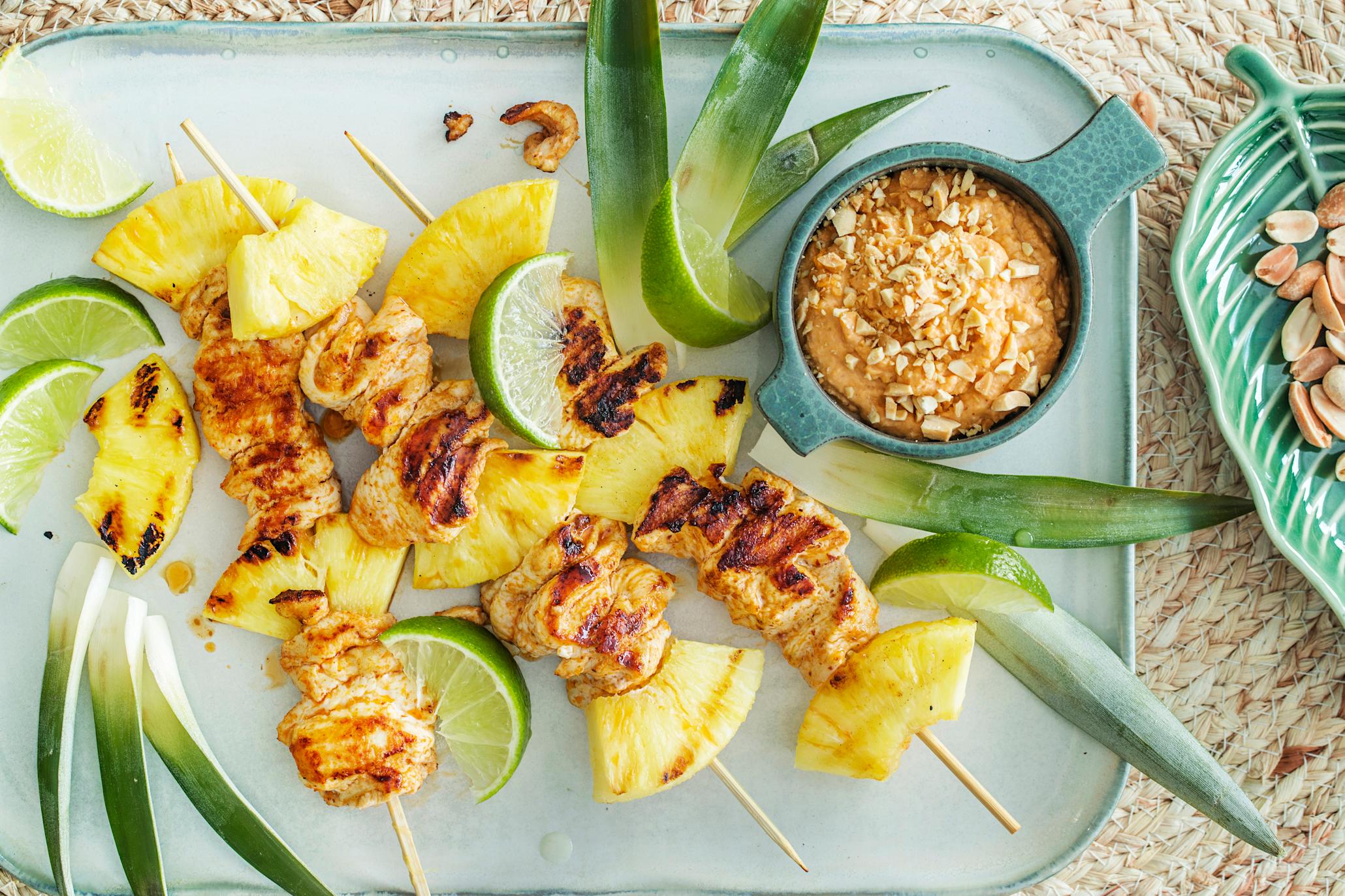 Grillet ananas med kylling på grillspyd med skål med peanøttsaus ved siden av