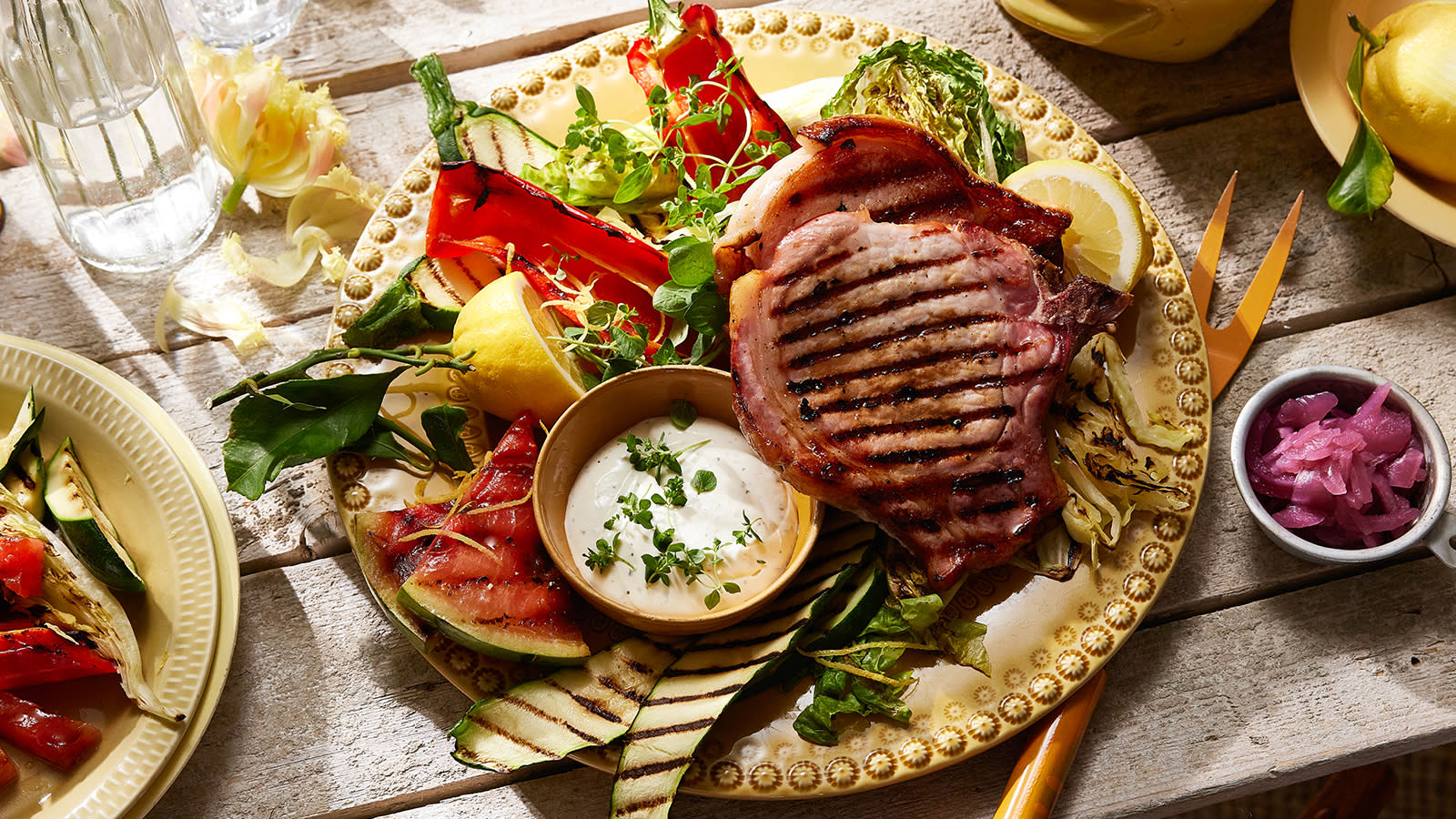 Sommerkoteletter med grillet sommersalat av squash, vannmelon, hjertesalat og snackpaprika servert på gult fat med små skåler tilbehør rundt.