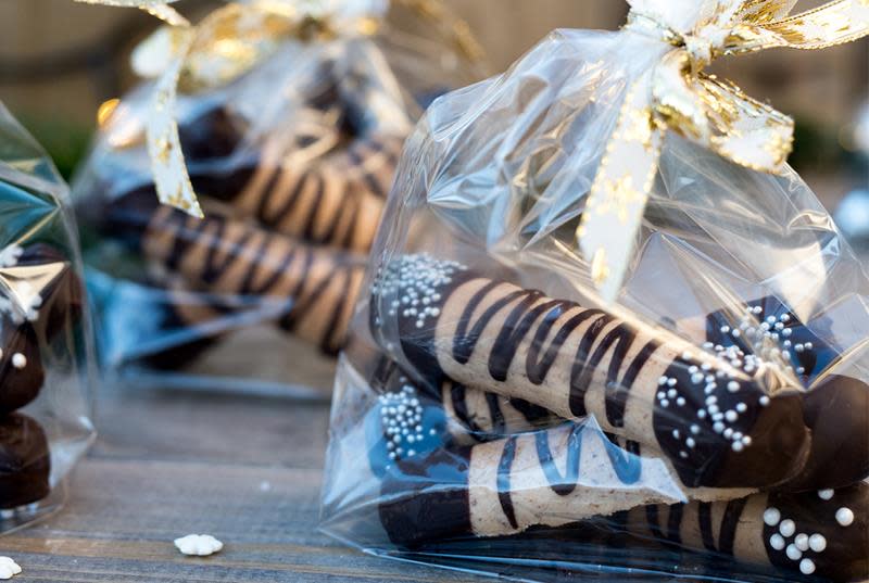 Hjemmelagede kransekakestenger dyppet i sjokolade i hver ende, og strødd med kakestrø. Kransekakestengene er pakket inn i julepyntede cellofanposer med gullbånd.