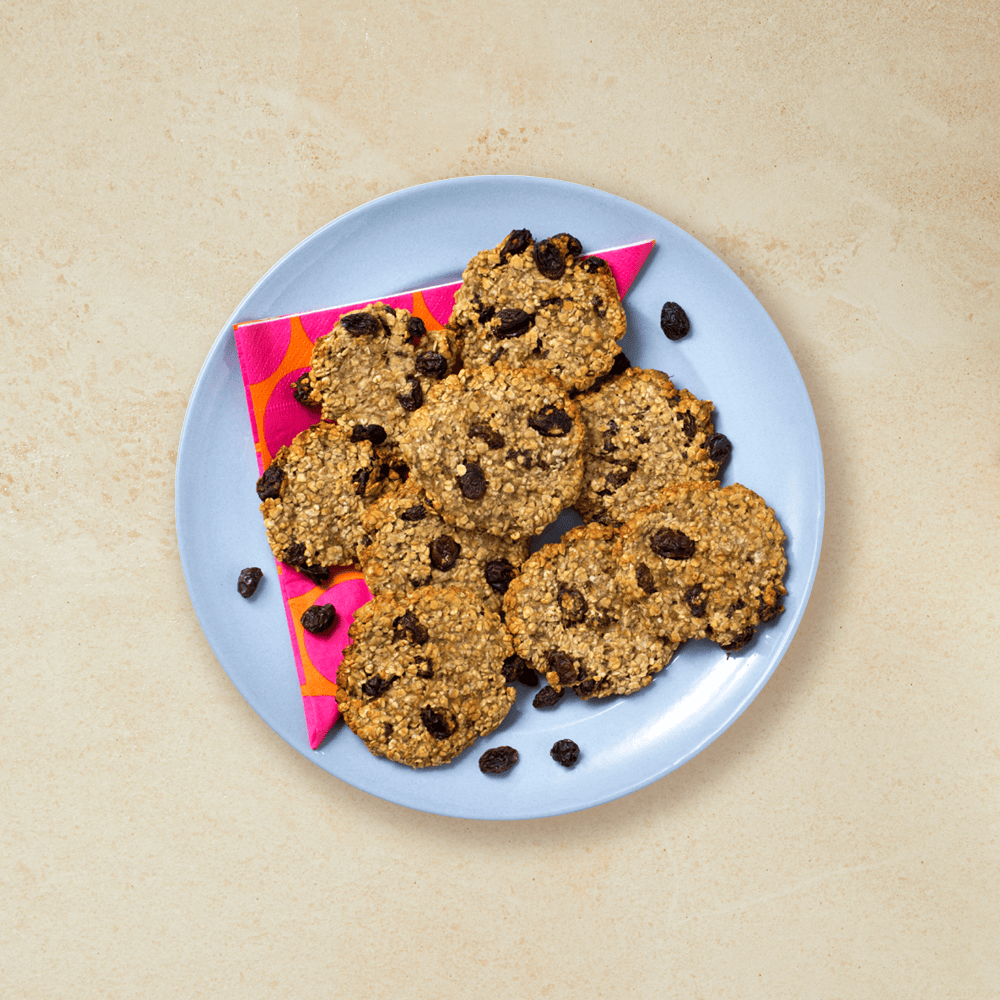 Enkle havrekjeks med banan og rosiner servert på blå tallerken med rosa- og oransjemønstret serviett.