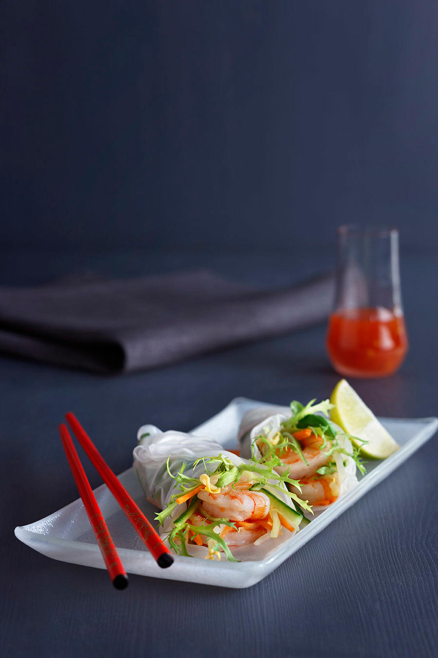 Sommerruller med scampi og grønnsaker, servert på hvitt firkantet fat, med sweet chilisaus i bakgrunnen.