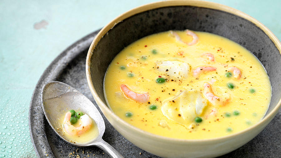 Kremet fiskesuppe med torsk og reker servert i mørk keramikkskål med friske erter og et dryss pepper.