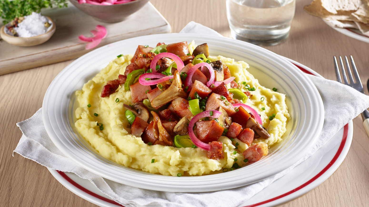 Brennende kjærlighet med pølser, bacon og hjemmelaget potetmos, servert med syltet rødløk på hvit tallerken på dekket middagsbord.