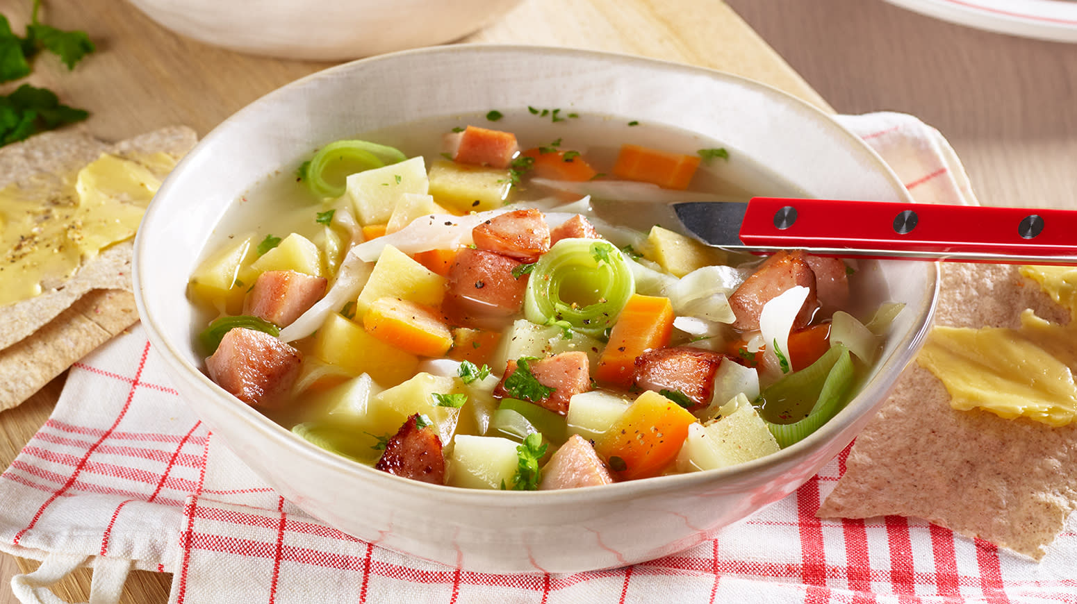 Betasuppe i hvit skål med rød skje, servert med flatbrød med smør oppå en hvit og rød tøyserviett.