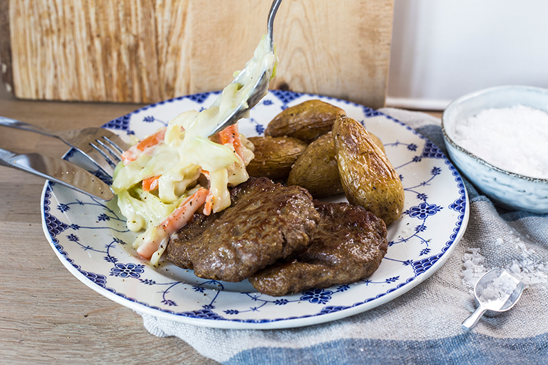 Karbonader med gulrot- og kålstuing, servert med kokte mandelpoteteter, på blåmønstret tallerken.