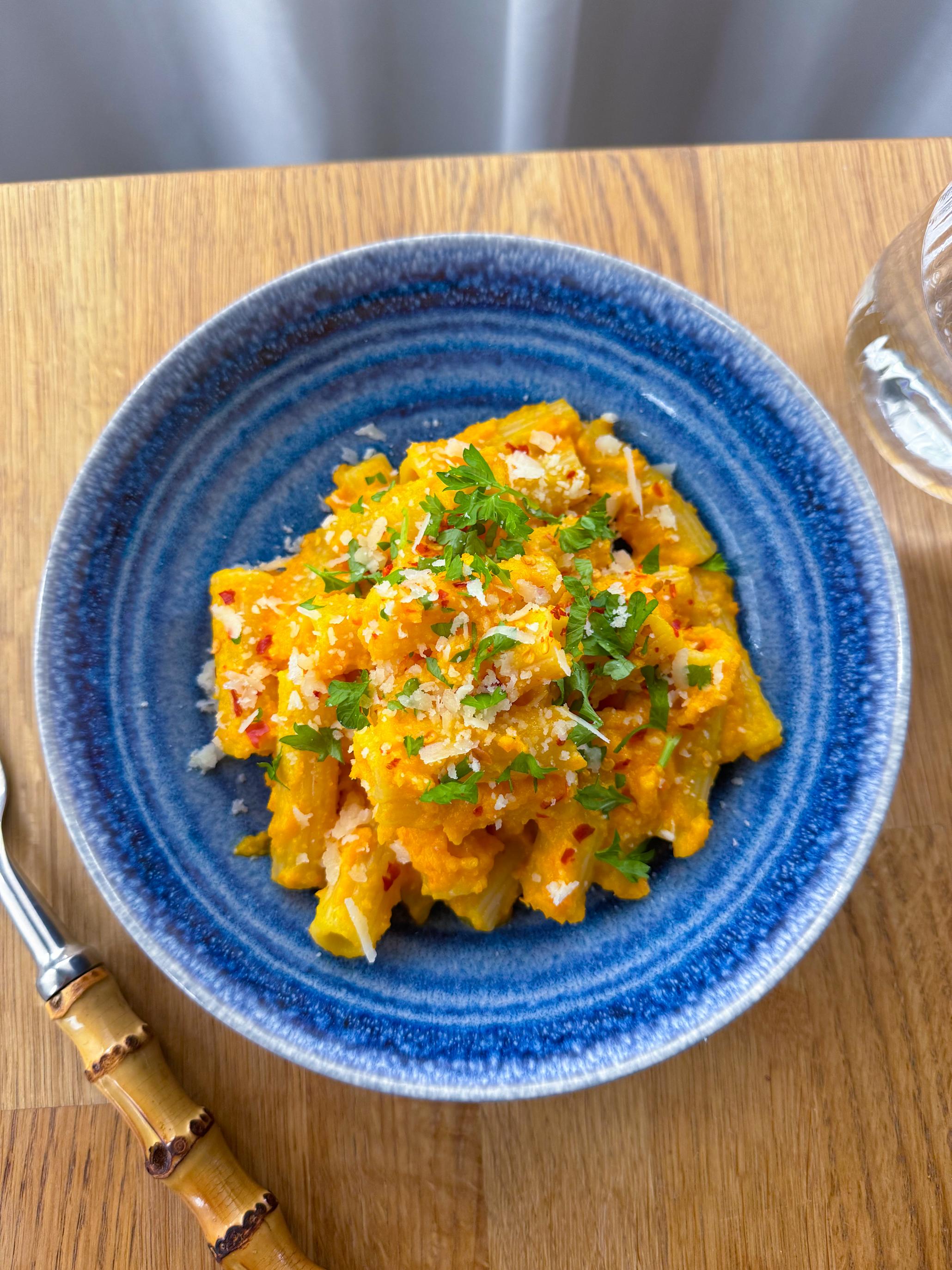 Gulrotpasta med kremet saus servert i blå skål med et dryss ferske urter og chiliflak over.