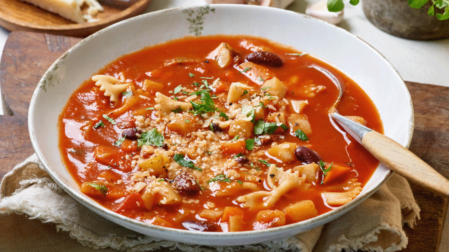 Skål med varm minestronesuppe fylt med pasta, bønner og grønnsaker, toppet med persille og revet ost.