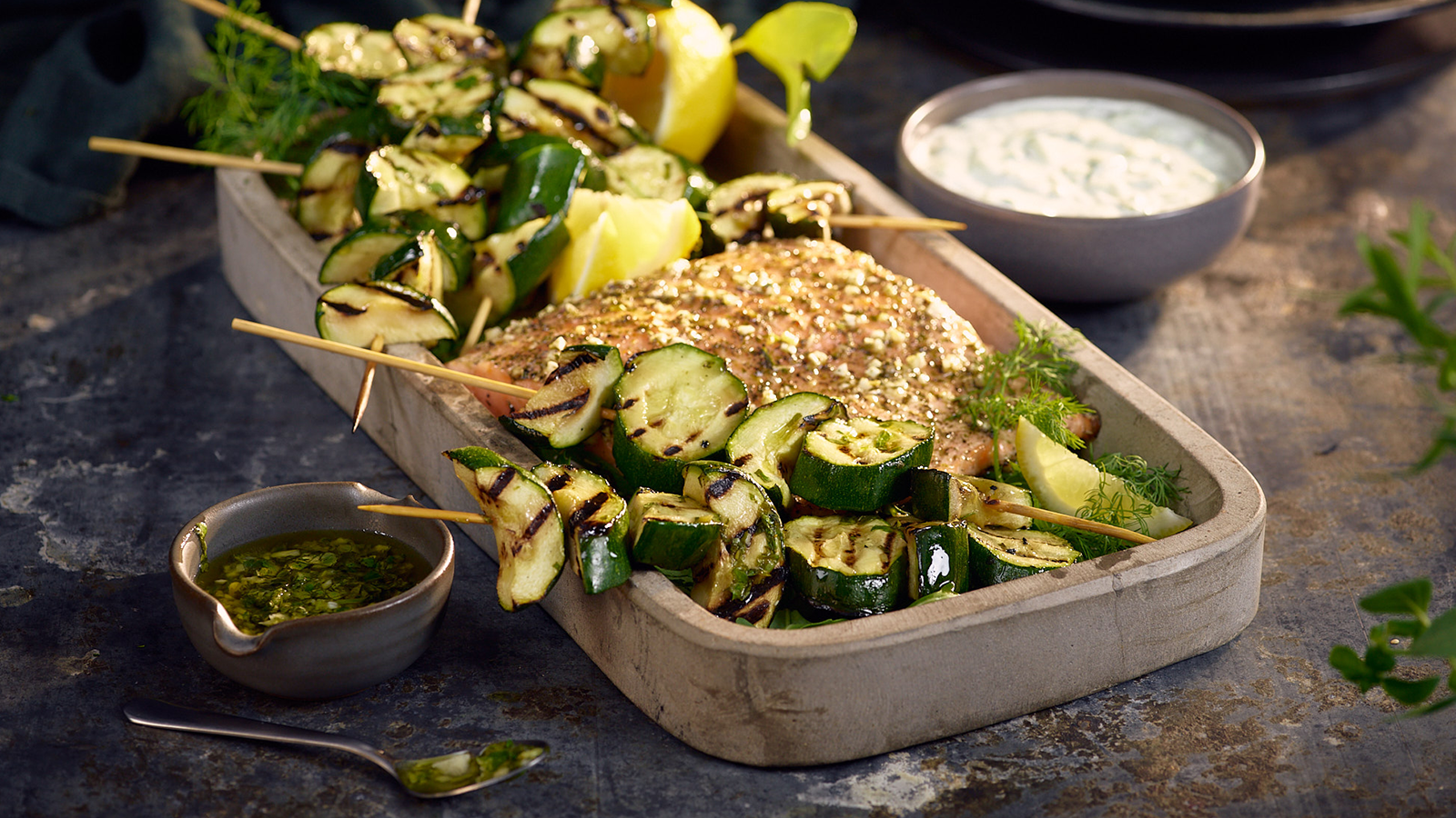 Grillet squash med laks og tzatziki servert i form. Små skåler med sauser rundt.