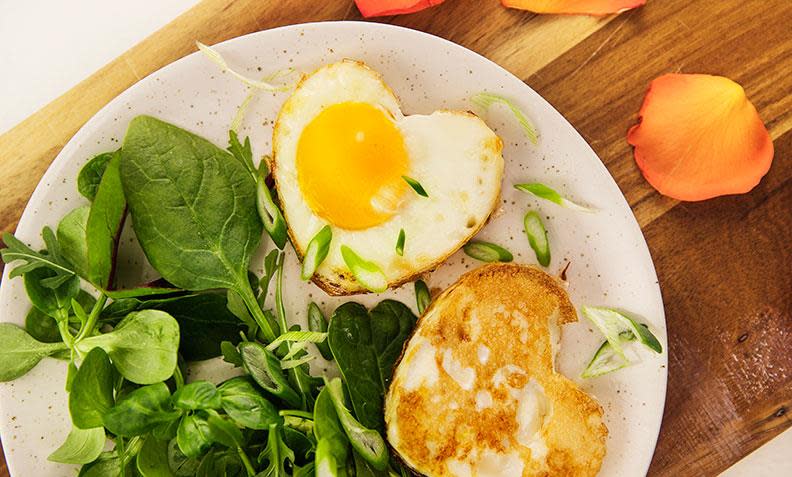 Hjerteegg i ovnen, hjerteformede speilegg laget i stekeovnen. Servert på hvit frokosttallerken med feldsalatmiks på siden, og vårløk på toppen.