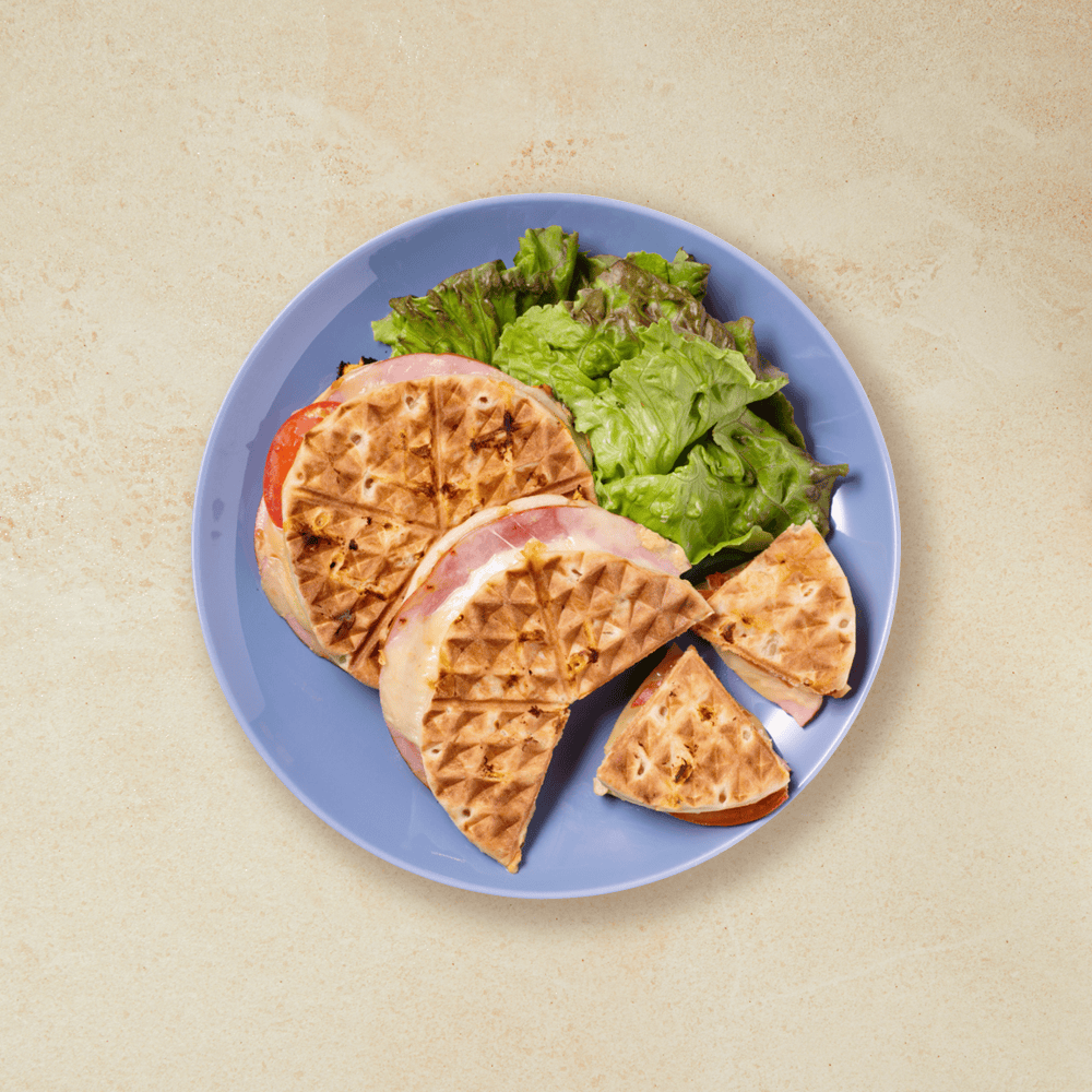 Runde toast med skinke, ost, tomat og salat, servert på en blå talleken